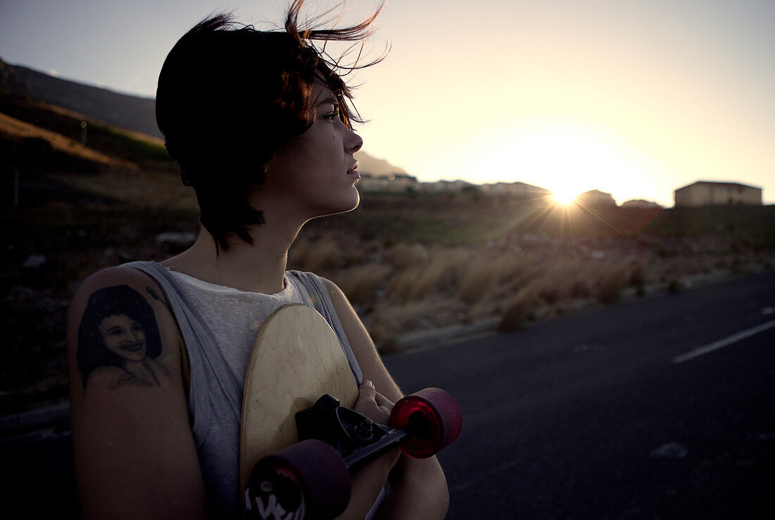 A young woman standing holding a skateboard.