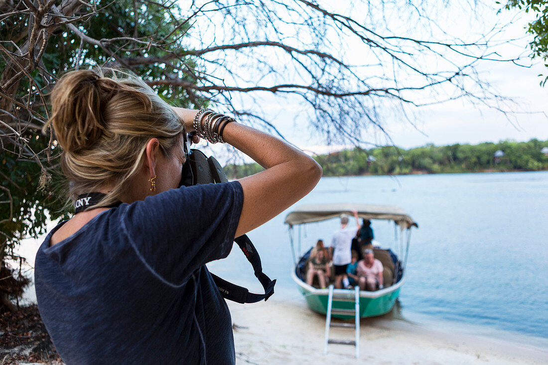 Eine Frau fotografiert mit ihrer Kamera ein Boot mit Passagieren auf dem Sambesi in Botswana