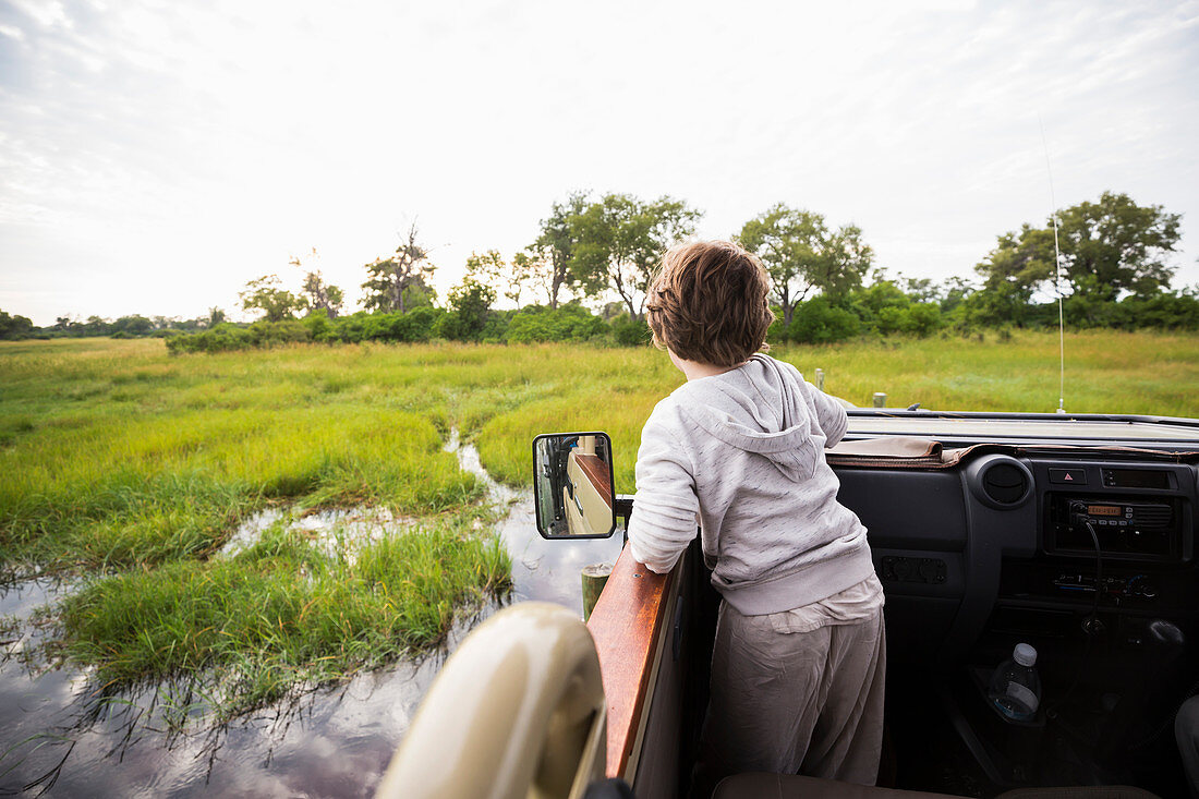 Ein sechsjähriger Junge in einem Safari-Jeep, der im Sumpfgebiet durchs Wasser fährt