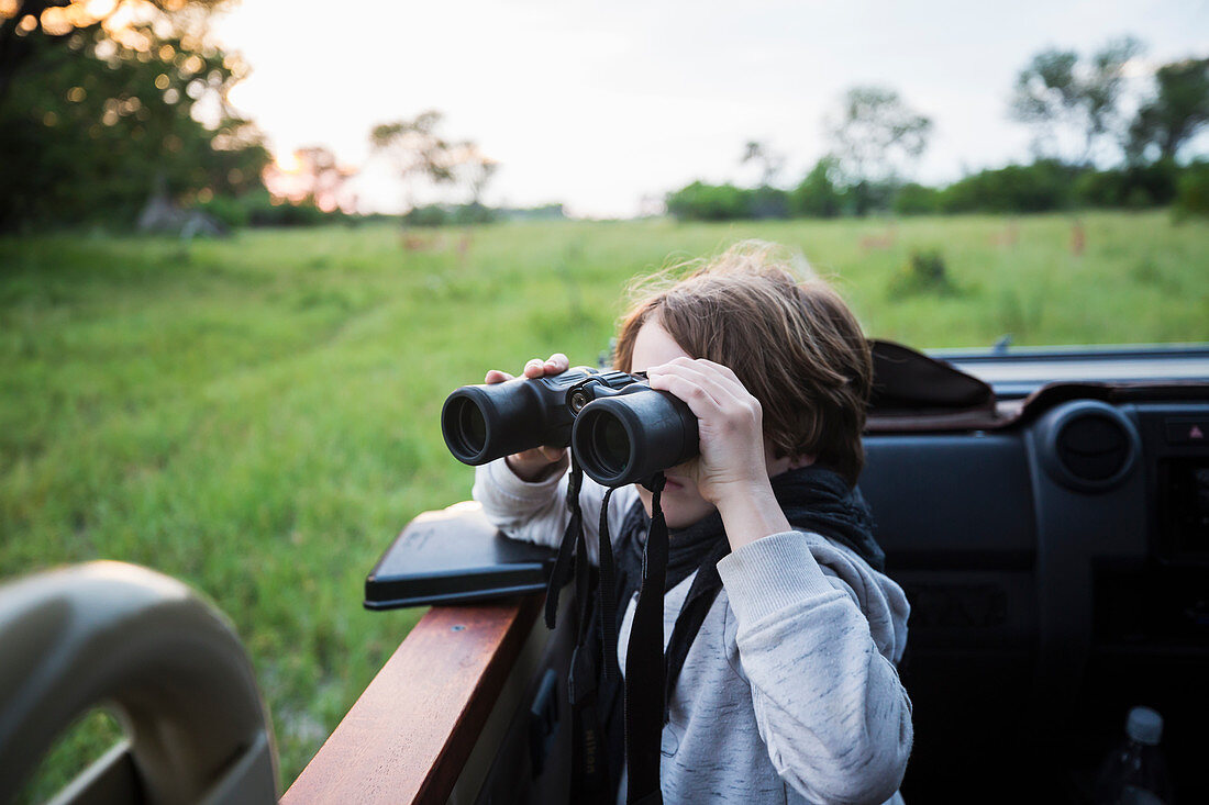 A six year old boy using binoculars seated in a safari jeep.