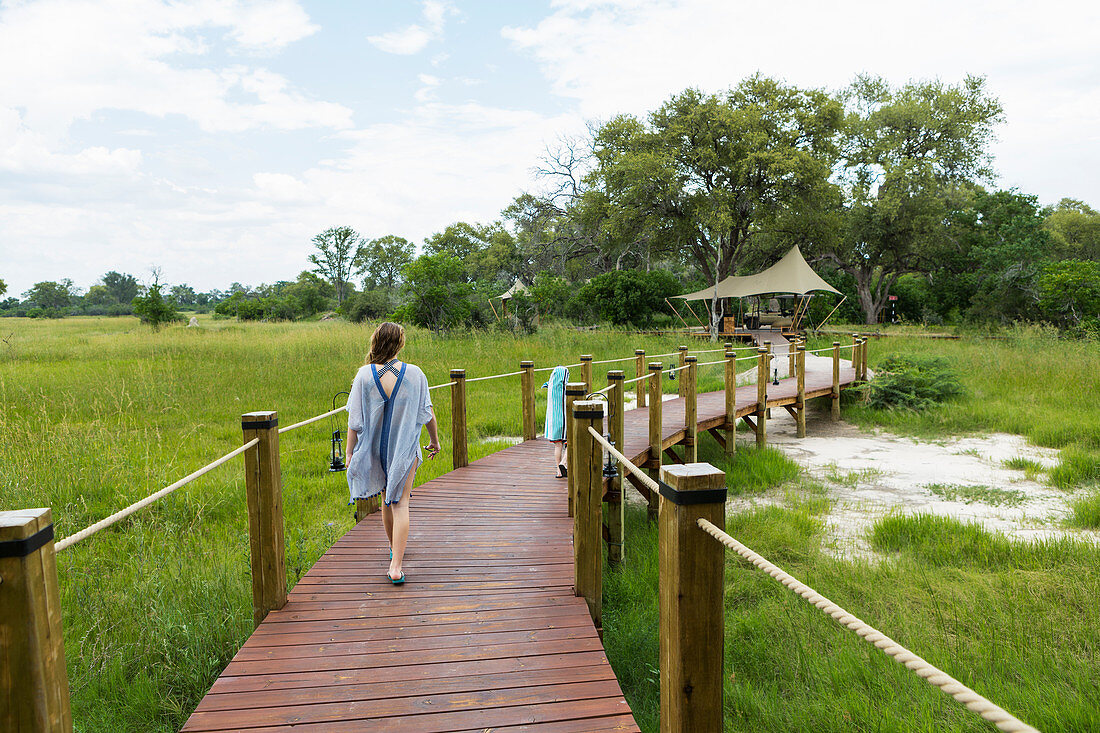 13 year old girl walking on wooden path, tented camp, Botswana
