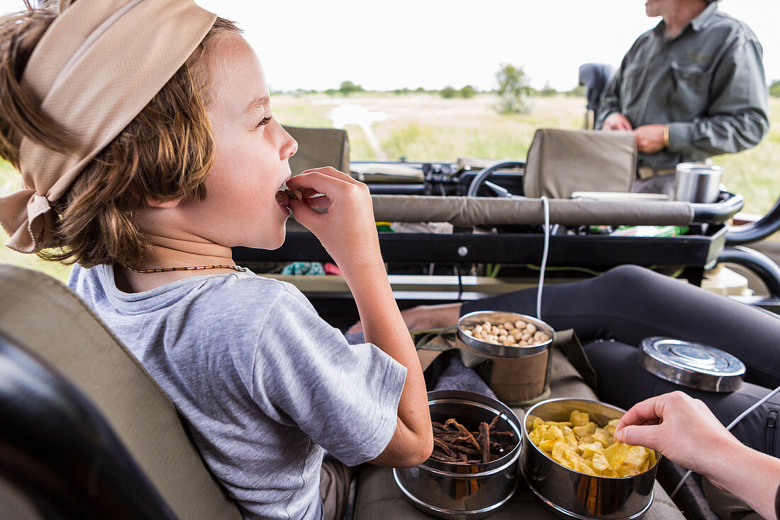 Sechsjähriger Junge isst Snacks im Safari-Jeep, Botswana