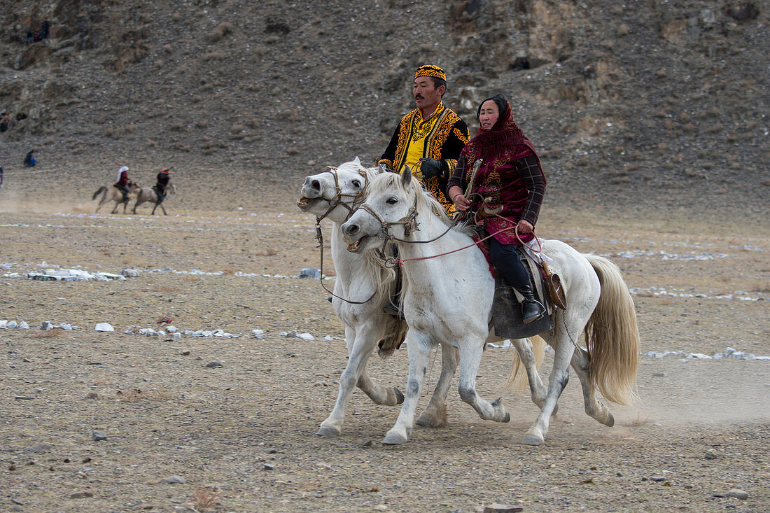 Ein Paar beim Spiel Kyz Kuar (Ein Mädchen einholen), einem traditionellen Reiterspiel, bei dem die Jungen von den Mädchen ausgepeitscht werden, wenn das Mädchen den Jungen fangen kann, beim Golden Eagle Festival (Adlerjägerfest) in der Nähe der Stadt Ulgii (Ölgii) in der Provinz Bajan-Ölgii in der westlichen Mongolei