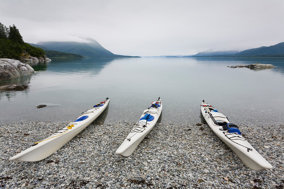 Sea kayaks on a remote beach, calm waters of an inlet on the Alaska coastline.