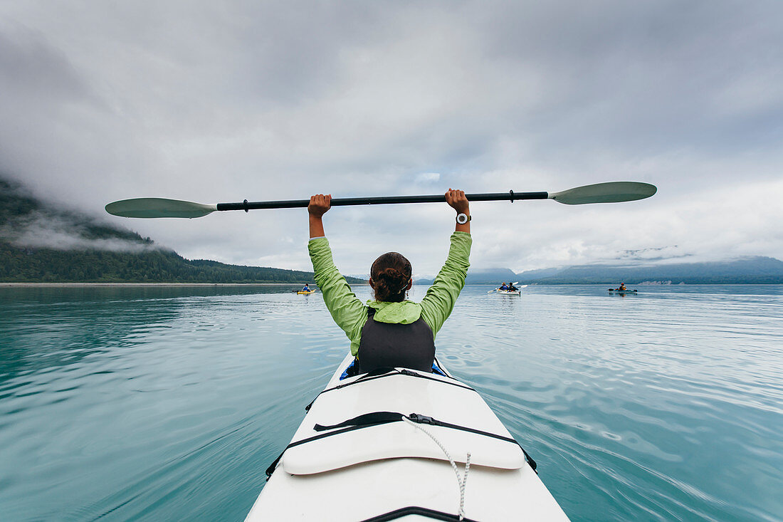 Frau hält Paddel über ihren Kopf, unberührtes Wasser von Muir Inlet in der Ferne, Glacier-Bay-Nationalpark, Alaska