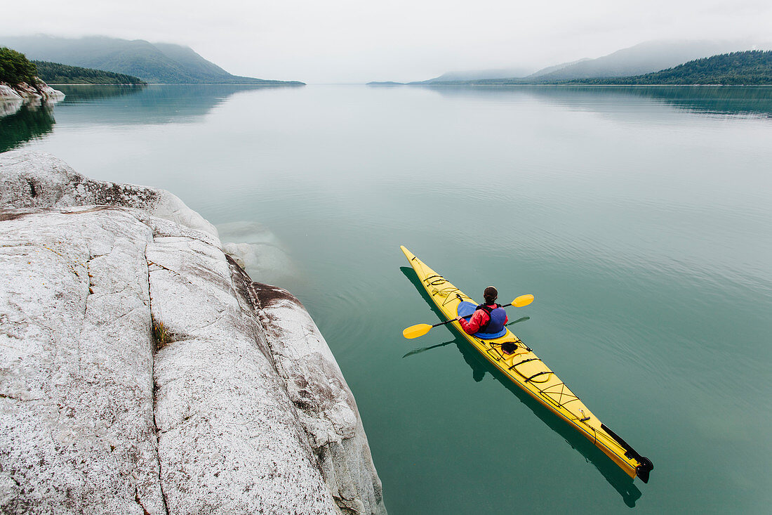 Frau unterwegs mit Kajak, unberührtes Wasser von Muir Inlet, bewölkter Himmel in der Ferne, Glacier-Bay-Nationalpark, Alaska