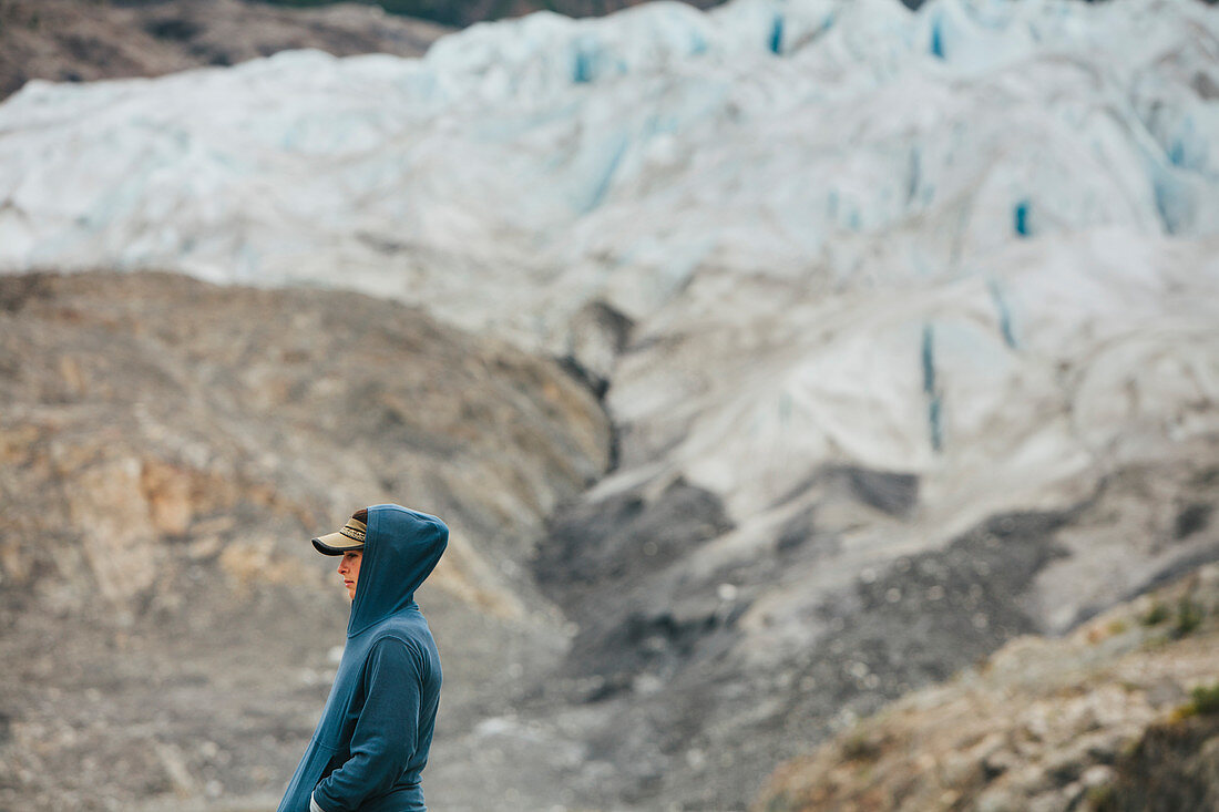 Junge Frau steht am Ende eines Gletschers an der felsigen Küste in Alaska