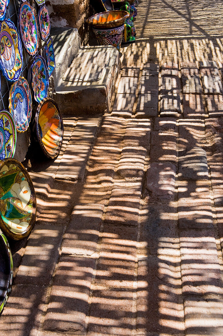 Shadows and shade patterns falling on a pavement, pottery bowls on display