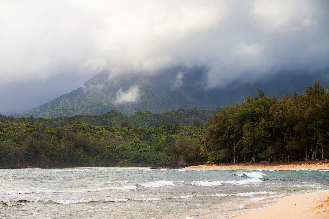 A sandy beach and waves breaking on shore, mountains in the mist above.