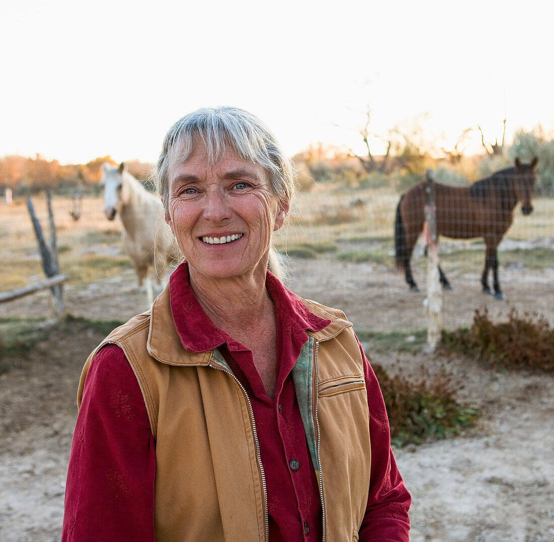 Reife Frau auf ihrem Grundstück in ländlicher Umgebung, Pferde auf einer Koppel