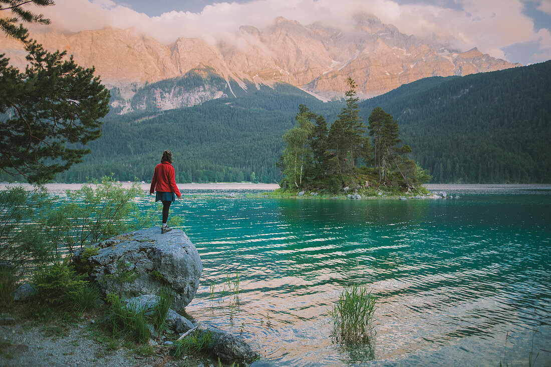 Deutschland, Bayern, Eibsee, Junge Frau steht auf einem Felsen am Eibsee in den bayerischen Alpen