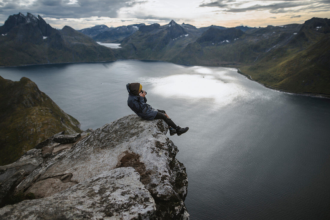 Norwegen, Senja, Mann fotografiert am Rande einer steilen Klippe auf dem Berg Segla sitzend