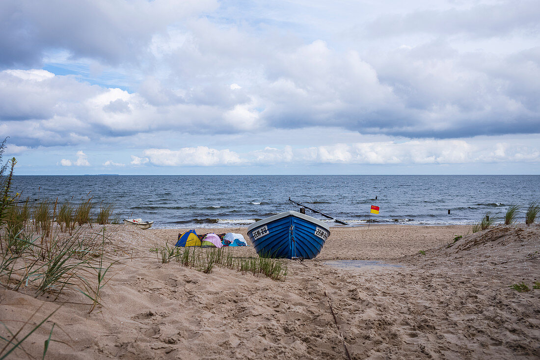 Altes Fischerboot am Strand von Bansin. Windiger Tag mit leichten Wellten bewölktem Himmel und Zelten am Strand, Usedom, Mecklenburg-Vorpommern, Deutschland