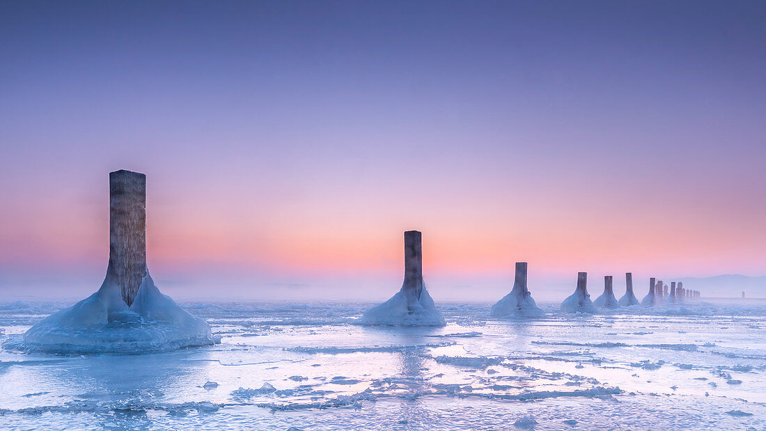 Icy winter morning in abandoned marina, wooden posts in the frozen lake at sunrise, Seeshaupt, Lake Starnberg, Bavaria, Germany