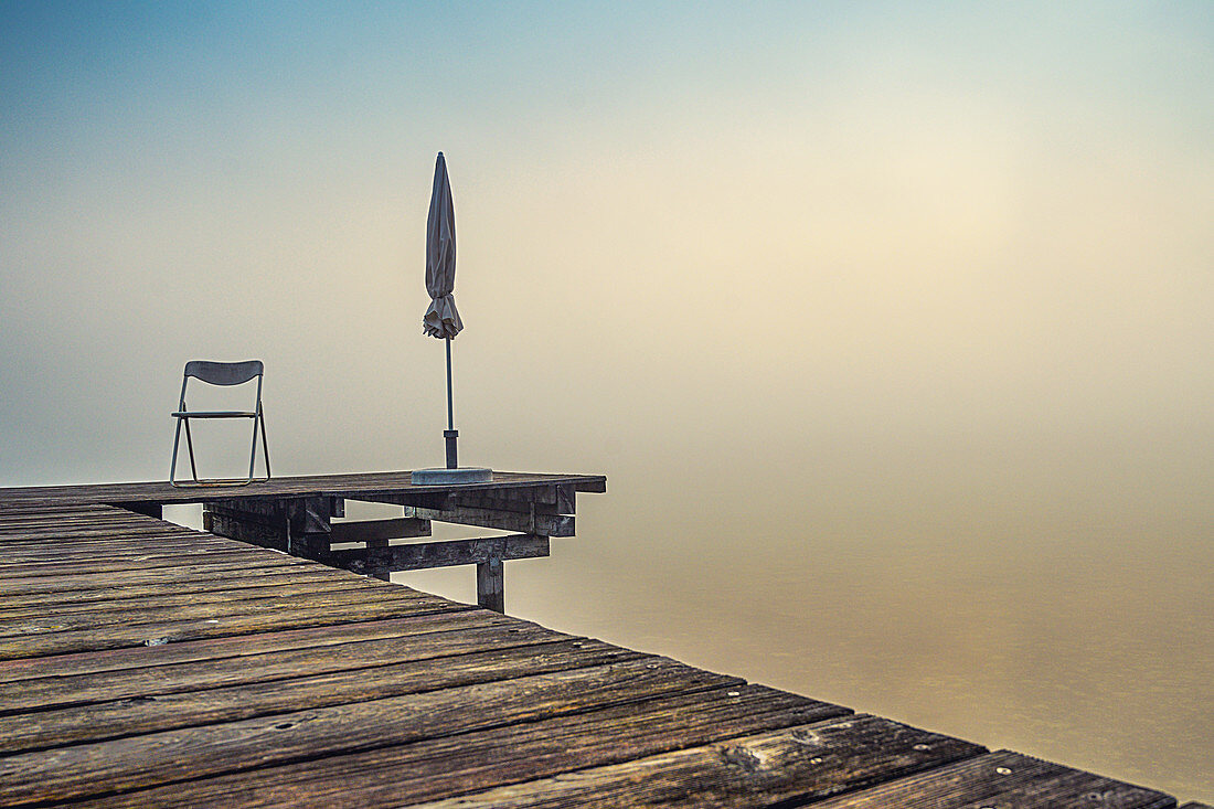 Jetty with folded parasols at misty sunrise on Lake Starnberg, Seeshaupt, Bavaria, Germany