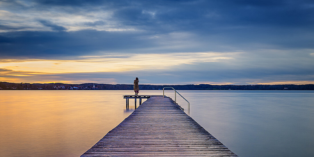 Frau auf Steg bei Sonnenuntergang am Starnberger See, St. Heinrich, Bayern, Deutschland