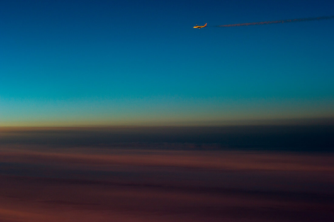 Flugzeug mit Kondensstreifen während der Abenddämmerung