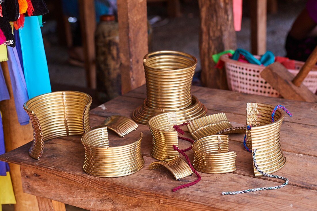False brass neck rings for tourists. Either you clip two parts to have a full collar or you adjust one single part with cords around you neck. In the background a real brass neck coil (approx. 3 kg ). The tourist shops are held by Kayan Lahwi women. The Long Neck Kayan (also called Padaung in Burmese) are a sub-group of the Karen ethnic from Burma. They wear spiral coils around their neck and lower legs.They are also nicknamed "giraffe women“. Pan Pet tourist market, Kayah state, Myanmar