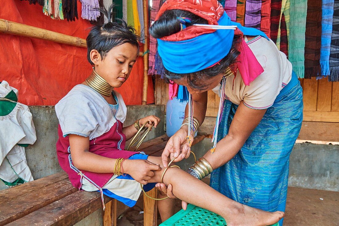 Kayan Lahwi woman putting a brass coil on the lower leg of her daughter. The Long Neck Kayan (also called Padaung in Burmese) are a sub-group of the Karen ethnic from Burma. Women wear spiral coils around their neck and lower legs.They are also nicknamed "giraffe women“. Pan Pet Region, Kayah State, Myanmar. 