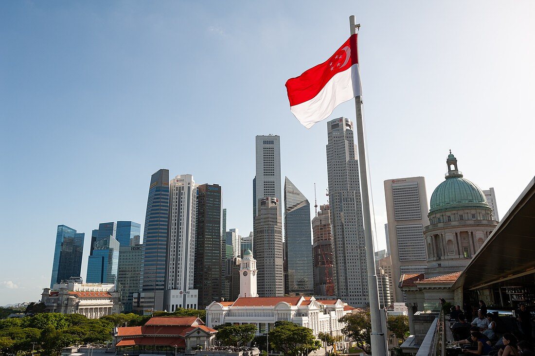 Singapore, Republic of Singapore, Asia - The red and white national flag waves in front of the city skyline of the central business district with the skyscrapers in Marina Bay and Raffles Place.