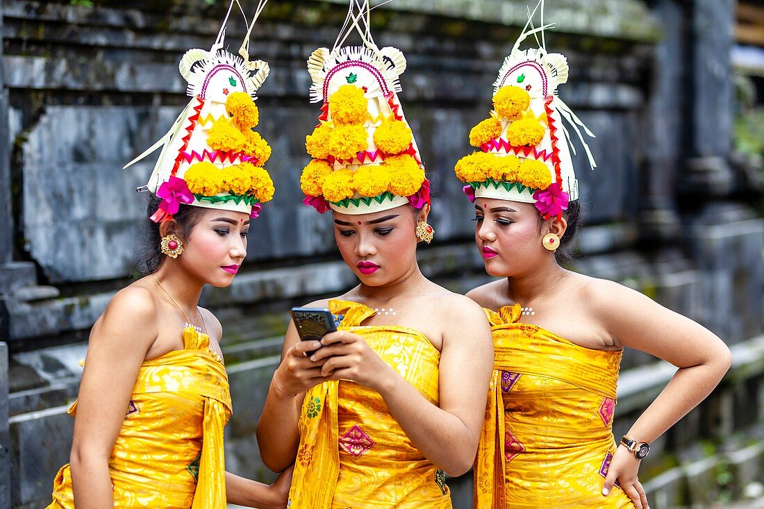 Young Balinese Hindu Females Looking At A Mobile Phone (Cellphone) At The Batara Turun Kabeh Ceremony, Besakih Temple, Bali, Indonesia.