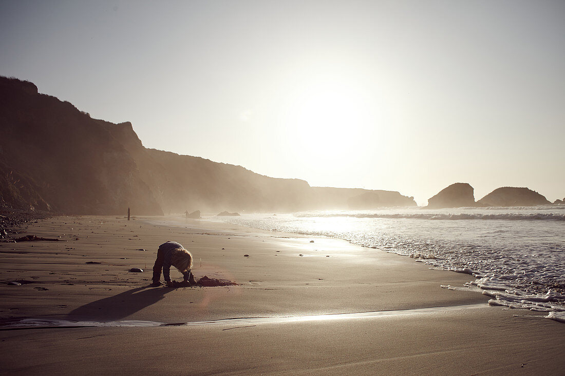 Small child digs in the evening light on Big Sur Beach, California, USA.