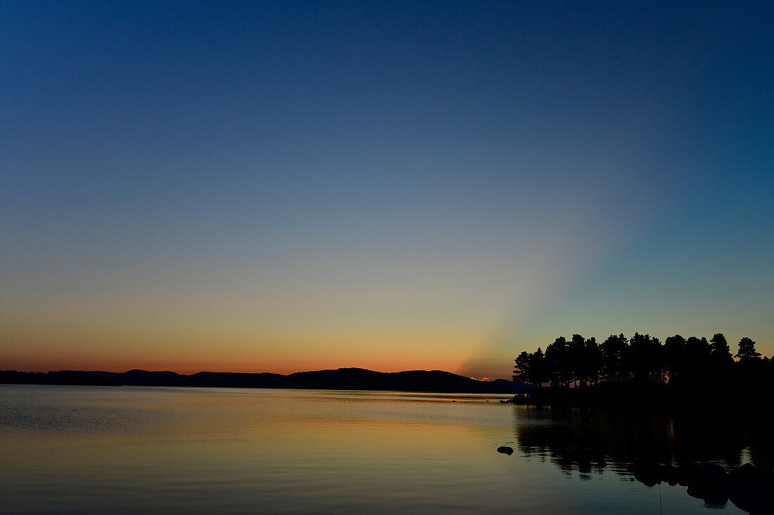 Späte Dämmerung mit Lichtstrahlen hinter einem Hügel, Orsjön, Tomterna, Västernorrland, Schweden