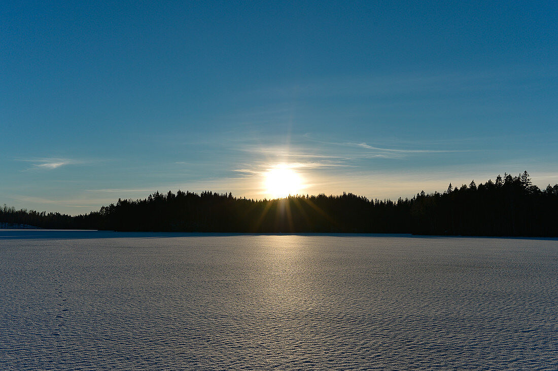 Untergehende Sonne über einem zugefrorenen See im Winter, Bolmsjön, Halland, Schweden