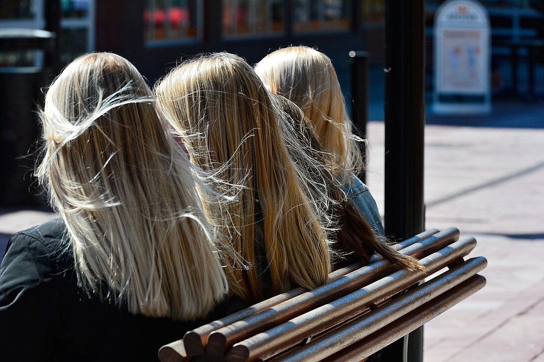 Four young women with typically Swedish blonde hair sit on a bench, Mora, Dalarna, Sweden