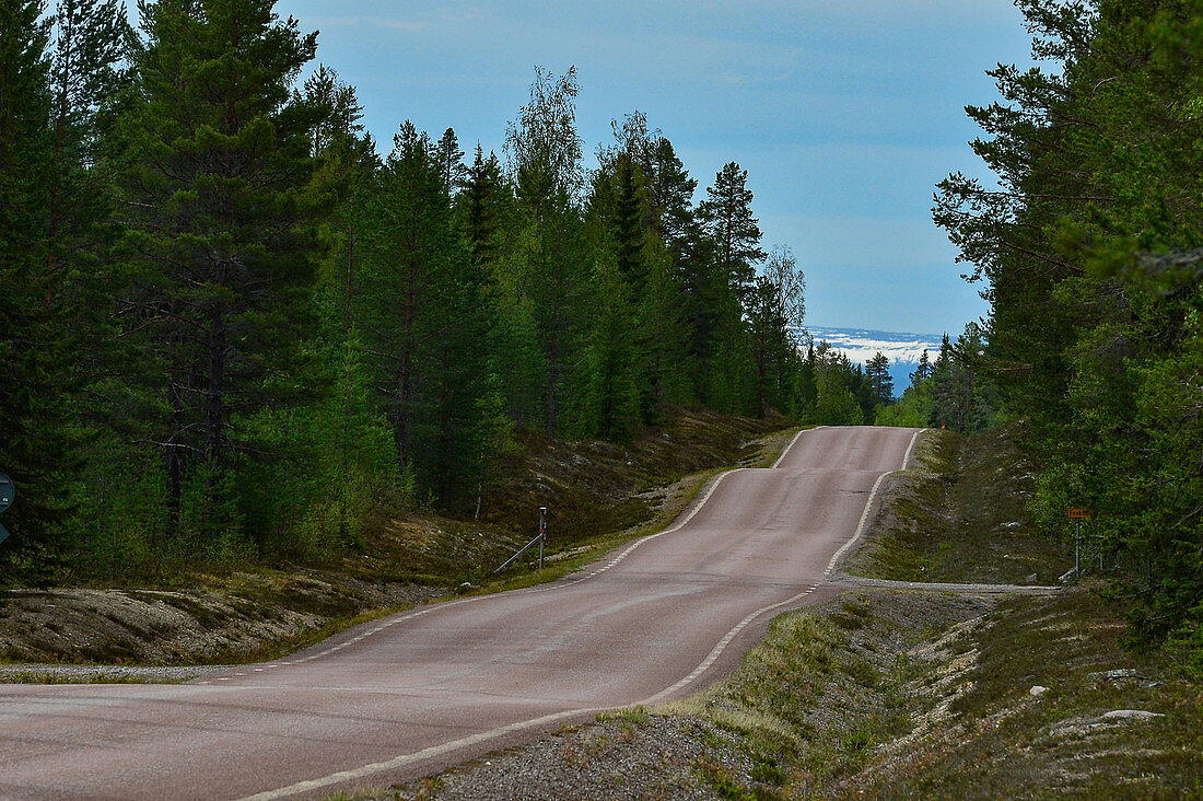 Gewellte Strasse mit schneebedeckten Bergen am Horizont, bei Tännäs, Jämtland, Schweden