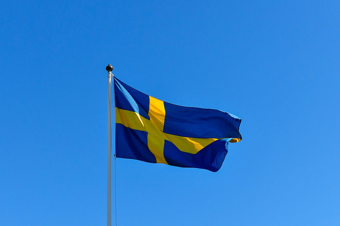 Die Flagge von Schweden flattert im Wind vor herrlich blauem Himmel, Bjuröklubb, Västerbottens Län, Schweden