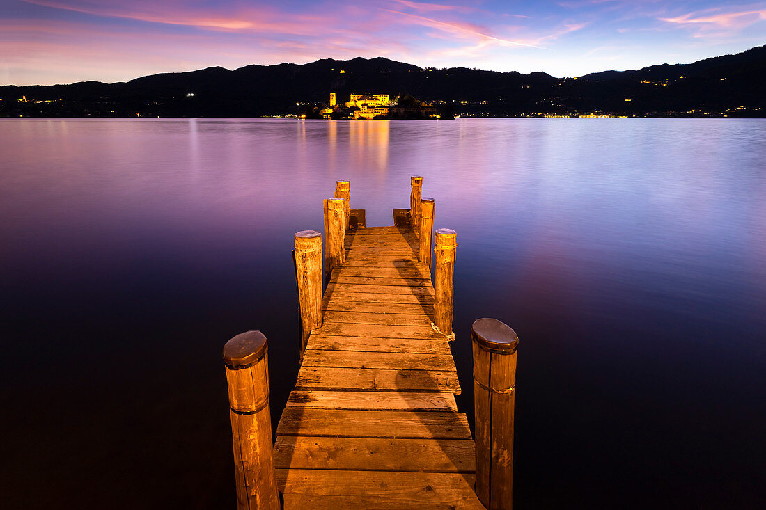 Sunset near a pier in front of San Giulio island and Lake Orta. Orta San Giulio, Orta Lake, Province of Novara, Piedmont, Italy.