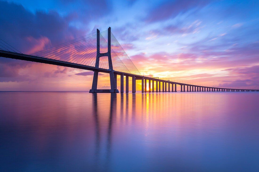 Ein farbenfroher Sonnenaufgang hinter der Vasco da Gama-Brücke, der sich auf dem Tejo spiegelt, Lissabon, Portugal, Europa