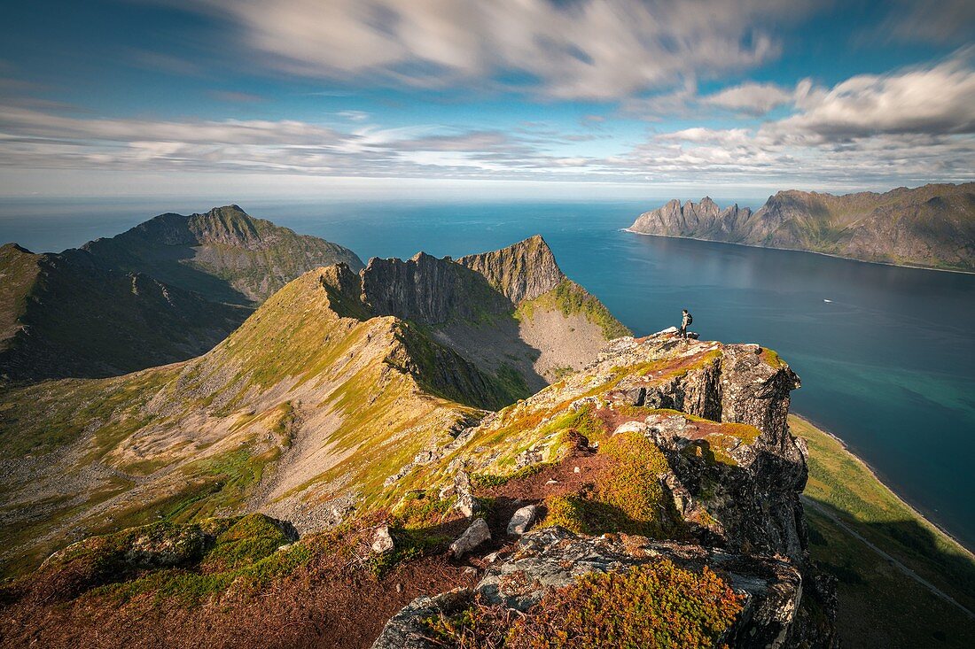 Wanderer auf dem Gipfel des Berges Husfjellet bei Sonnenuntergang, Fjorde und Berge Im Hintergrund, Senja, Norwegen