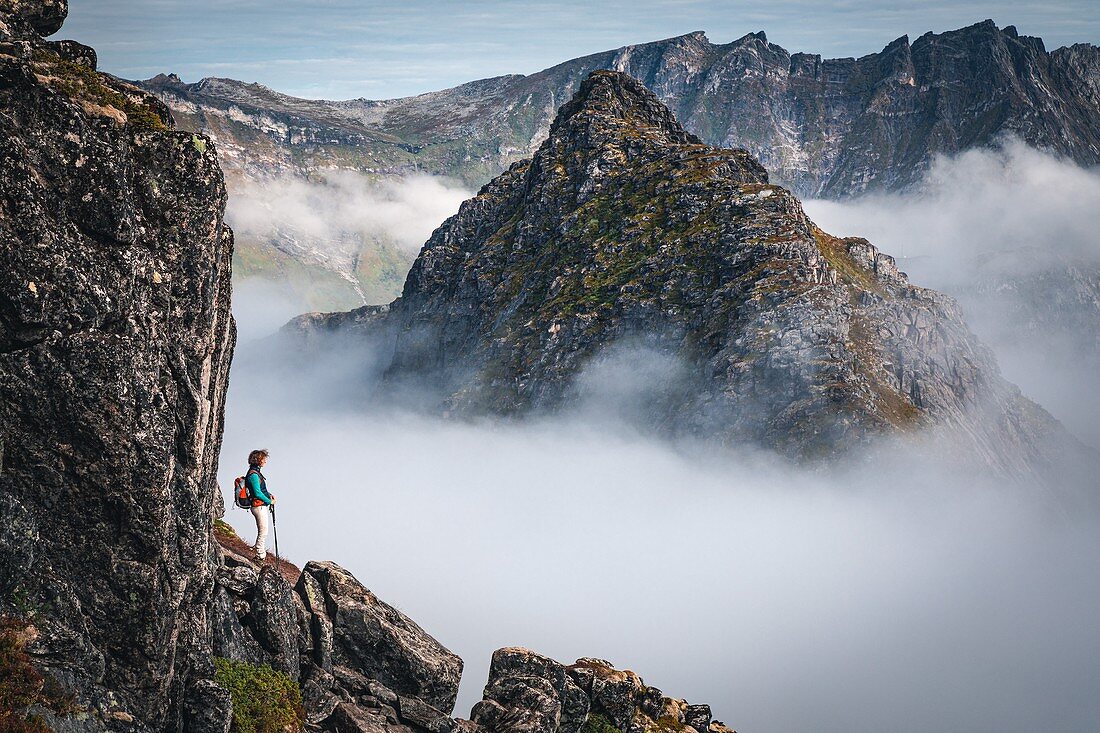 HIKER CONTEMPLATING THE MOUNTAINS EMERGING FROM A SEA OF CLOUDS, MOUNT HESTEN, FJORDGARD, SENJA, NORWAY