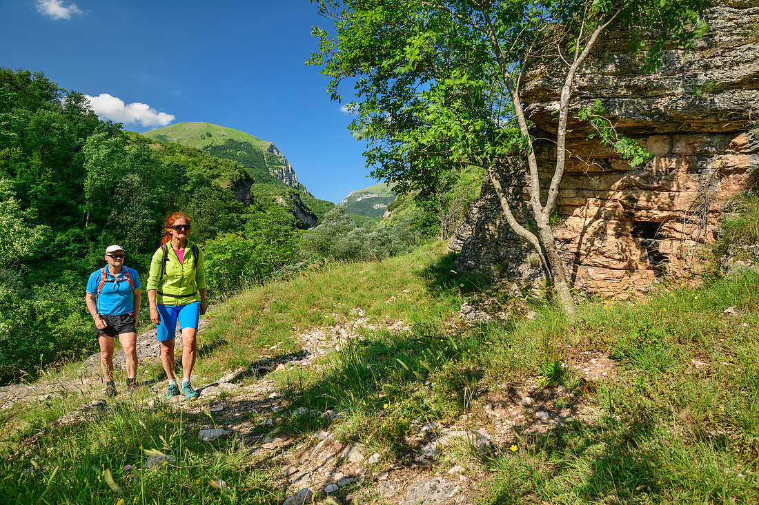 Man and woman hiking past rock face, Grande Anello dei Sibillini, Sibillini Mountains, Monti Sibillini, National Park Monti Sibillini, Parco nazionale dei Monti Sibillini, Apennines, Marche, Umbria, Italy