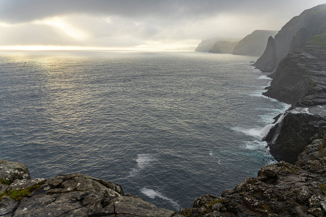 Steep coast in the west of the island of Vágar with the waterfall Bøsdalafossur and the rock needle Geitaskoradrangur near the largest lake in the Faroe Islands, Leitisvatn, Faroe Islands