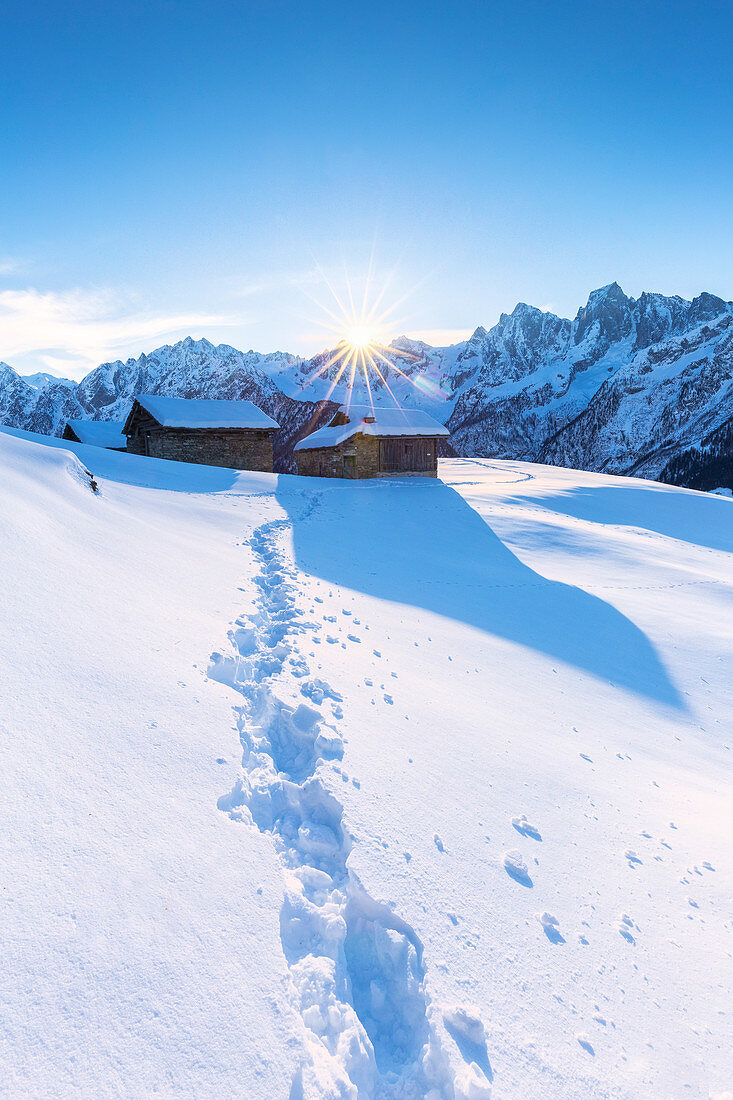 Fußabdruck im Neuschnee mit traditioneller Hütte im Hintergrund, Soglio, Bergell-Tal, Kanton Graubünden, Schweiz, Europa