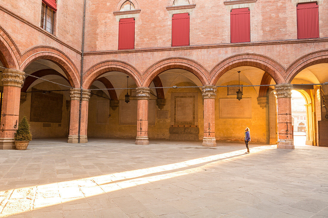 Tourist admiring Accursio palace interior courtyard. Maggiore square, Bologna, Emilia Romagna, Italy, Europe.