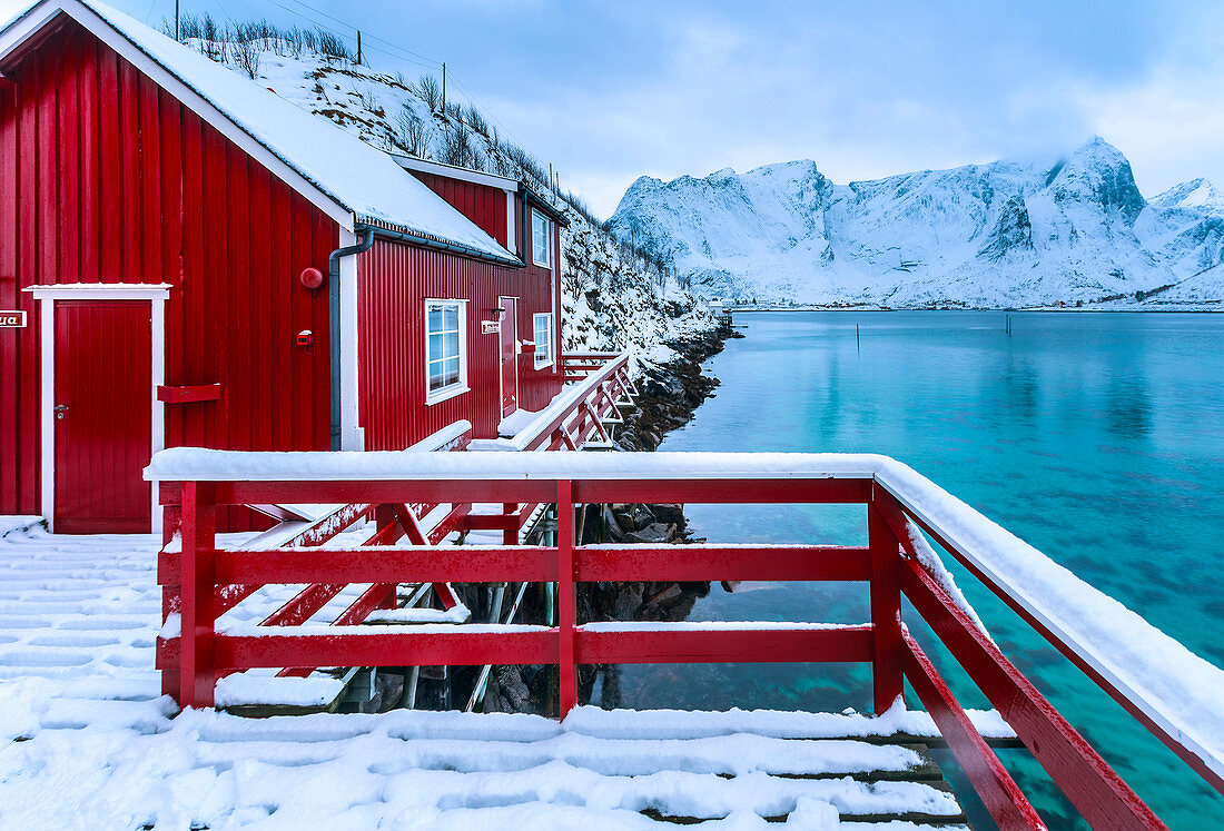 Typisches rotes Haus spiegelt sich im Meer, Reine, Lofoten, Norwegen