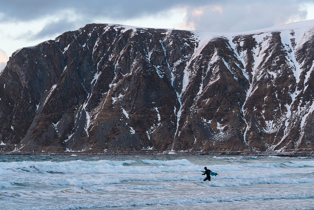 Mann beim Surfen im Meer im Winter, Strand von Skagsanden, Flakstad, Nordland, Nordnorwegen, Norwegen
