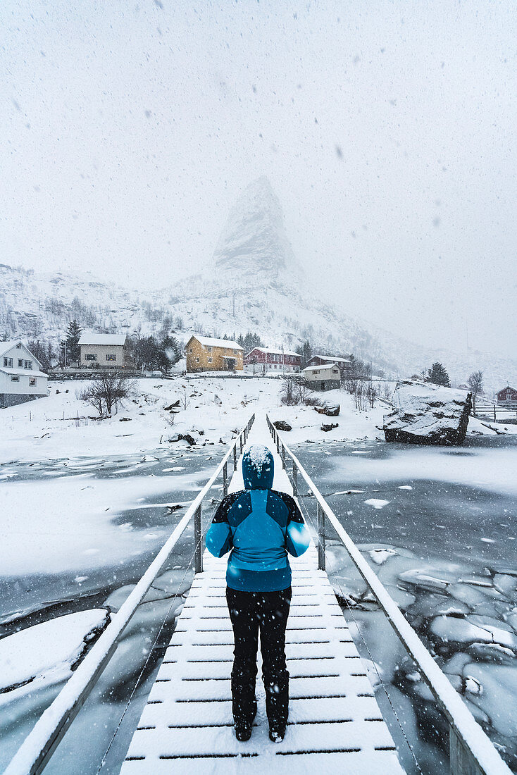 Frau steht auf einer Holzbrücke im Schnee mit Blick Richtung Hammarskaftet, Reine, Nordland, Nordnorwegen, Norwegen