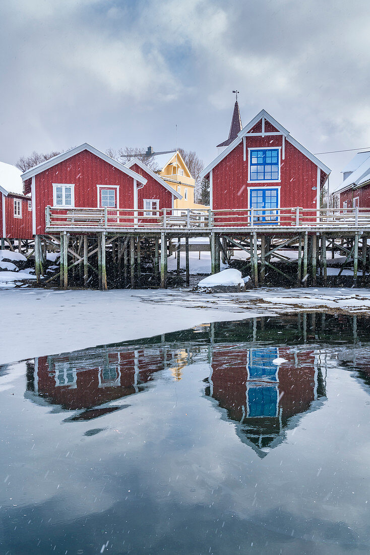 Traditionelle 'Rorbu'-Häuser spiegeln sich auf dme gefrorenen Fjord wider, Reine, Lofoten, Nordland, Nordnorwegen, Norwegen