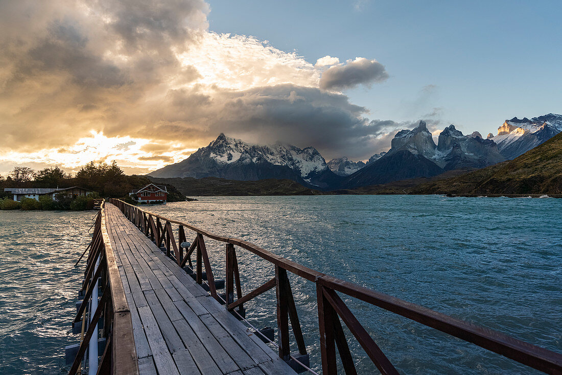 Wooden bridge on Lake Pehoé with Cerro Paine Grande and Paine Horns in the background at sunset. Torres del Paine National Park, Ultima Esperanza province, Chile.