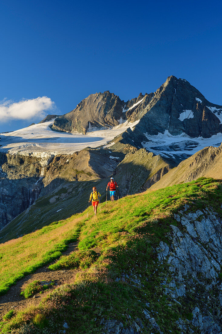 Man and woman hiking down from the Figerhorn, Grossglockner in the background, Figerhorn, Glockner Group, Hohe Tauern, Hohe Tauern National Park, East Tyrol, Austria