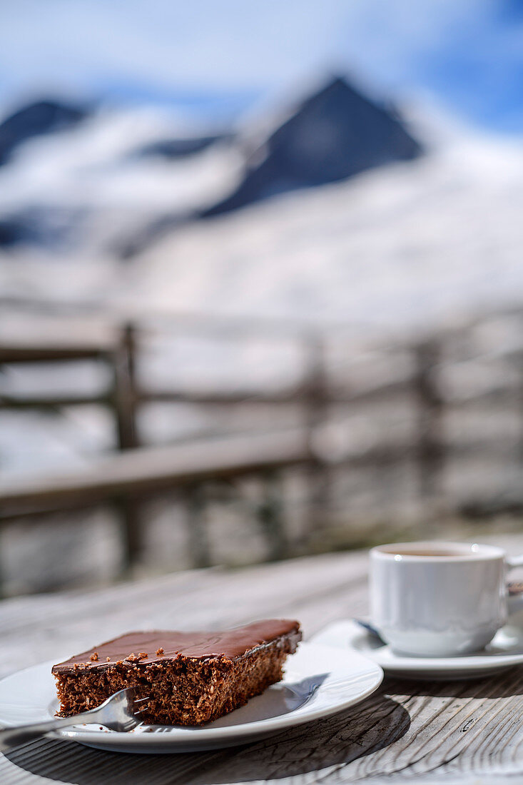 Coffee and cake with mountain out of focus in the background, Neue Prager Hütte, Venedigergruppe, Hohe Tauern, Hohe Tauern National Park, East Tyrol, Austria