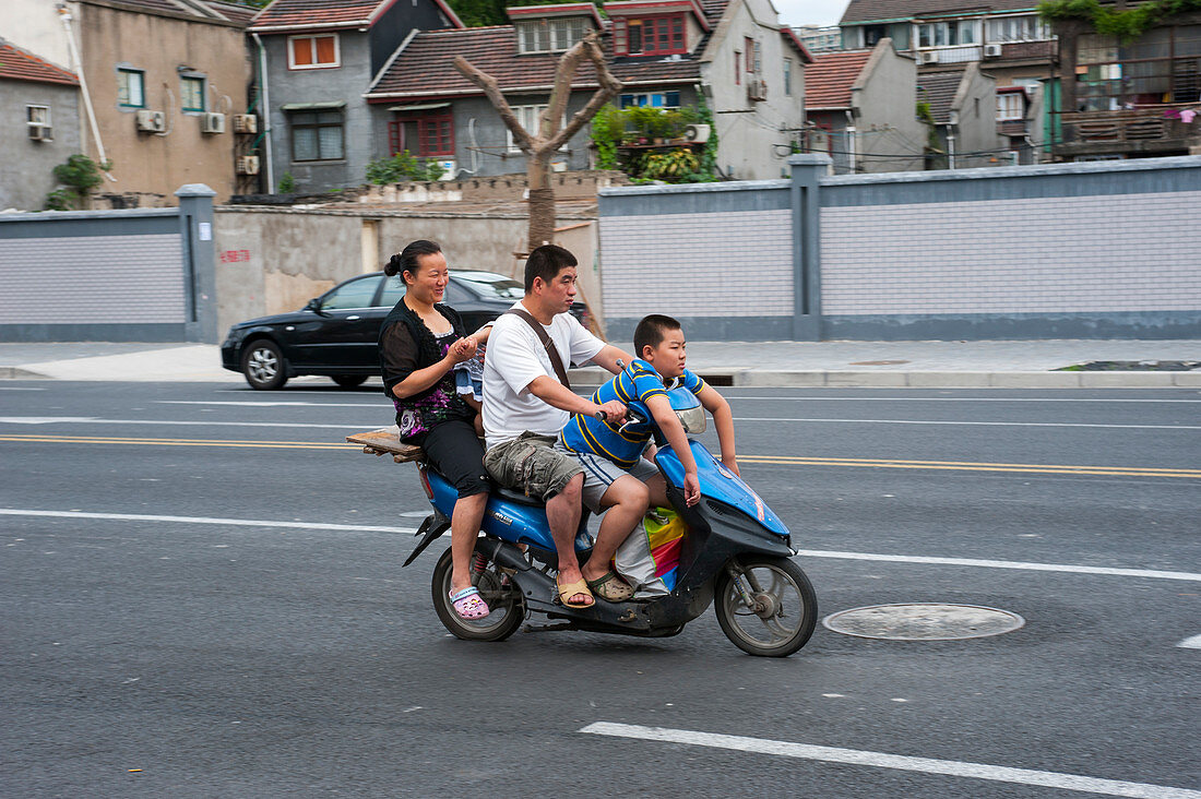 Street scene with a family riding on a motor scooter in Shanghai, China.