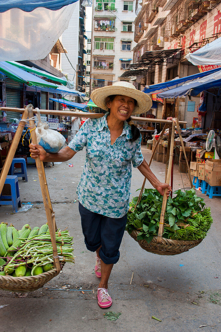 A woman is carrying produce on a carrying pole, also called a shoulder pole, over the shoulders in the city of Fengdu on the Yangtze River in China.