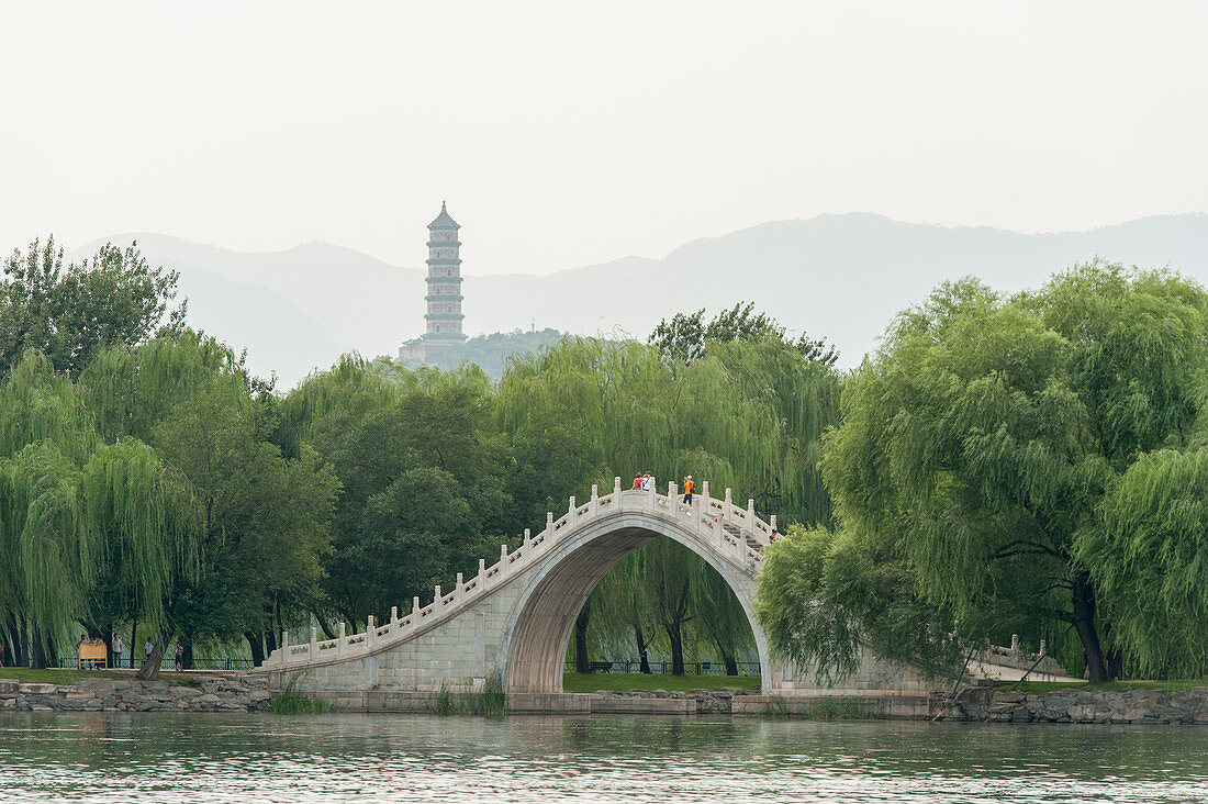 Blick über den Kunming-See in Richtung einer Steinbrücke und des Jade Spring Hill mit der Jade Peak Pagode im Sommerpalast, dem kaiserlichen Garten der Qing-Dynastie in Peking, China.