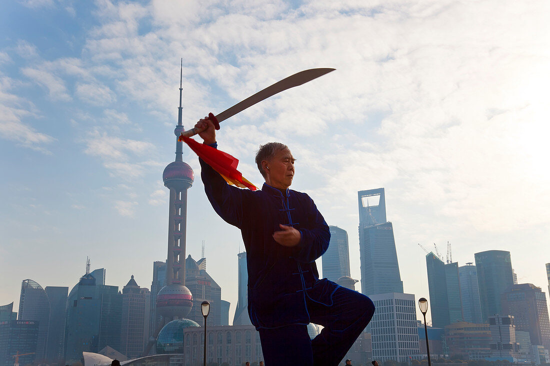 Practising Tai Chi with sword, with Pudong skyline, early morning, Shanghai, China